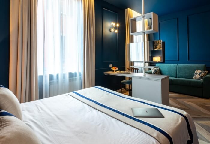 camera d’albergo con pareti blu scuro avvolgenti e pavimentazione e biancheria letto a contrasto in legno chiaro bicromatico per un effetto elegante