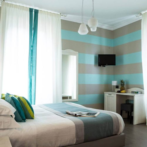 camera di hotel a tema marinaro con pareti a righe orizzontali grigio e verde marino con tendaggi e copriletti in tinta