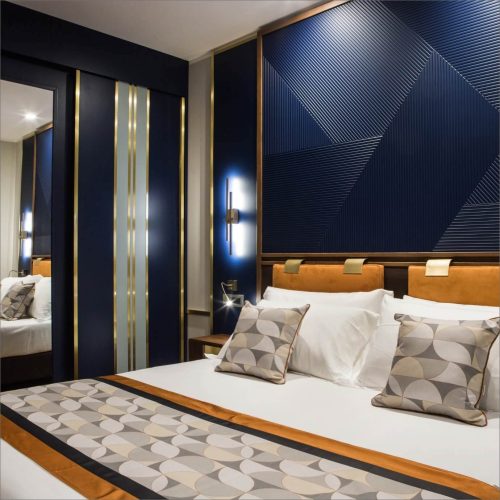 porzione di letto bianco con spalliera e rivestimento delle pareti con materiali lucidi con disegni optical blu scuro